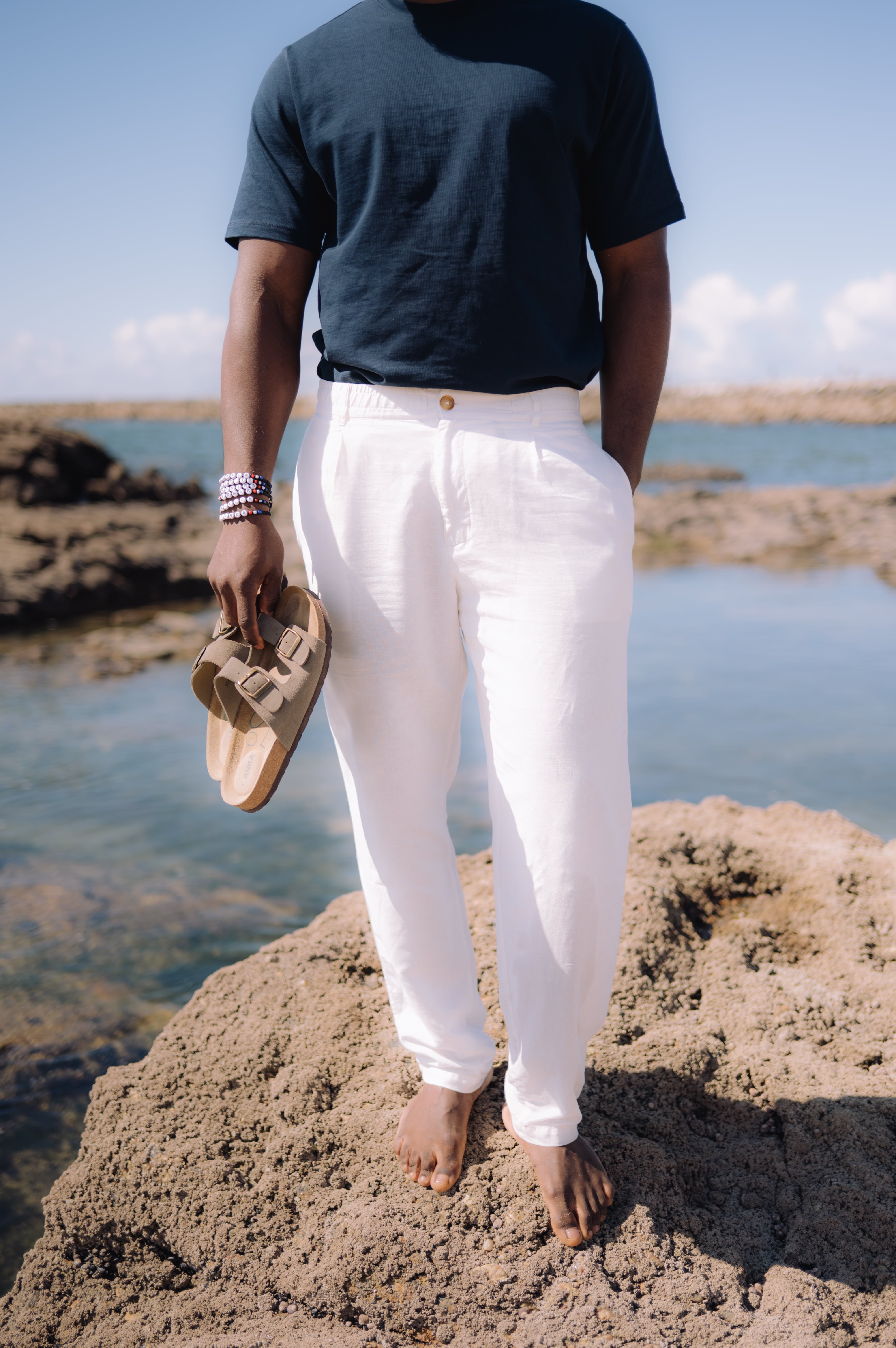 Homem, na praia sob as rochas, com calças de linho.
